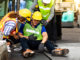 First Aid. Engineering supervisor talking on walkie talkie communication while his coworker lying unconscious at industrial factory. Professional engineering teamwork concept.